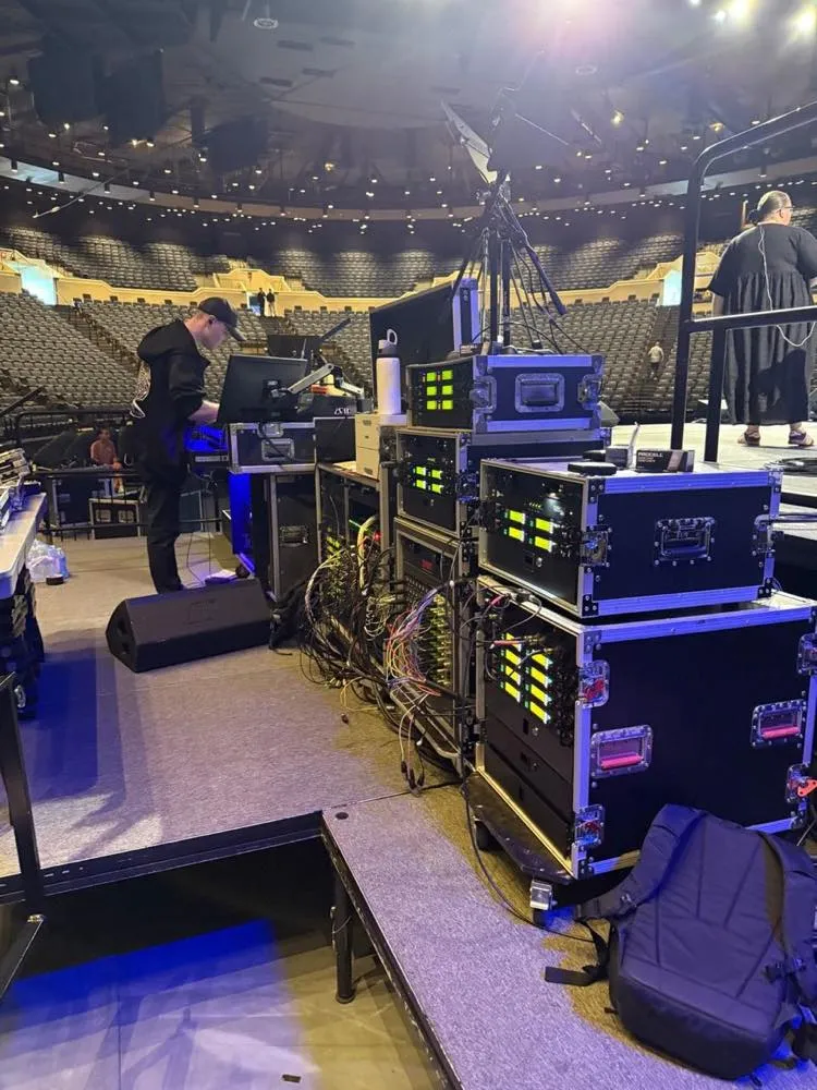Phase 3 Live stage tech with audio drive racks side-stage during an arena event setup