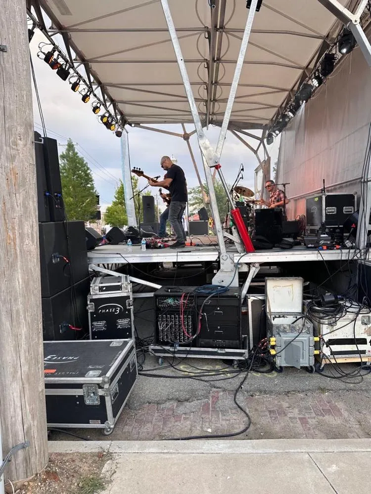 Backstage view of a daytime outdoor concert on a covered stage produced by Phase 3 Live
