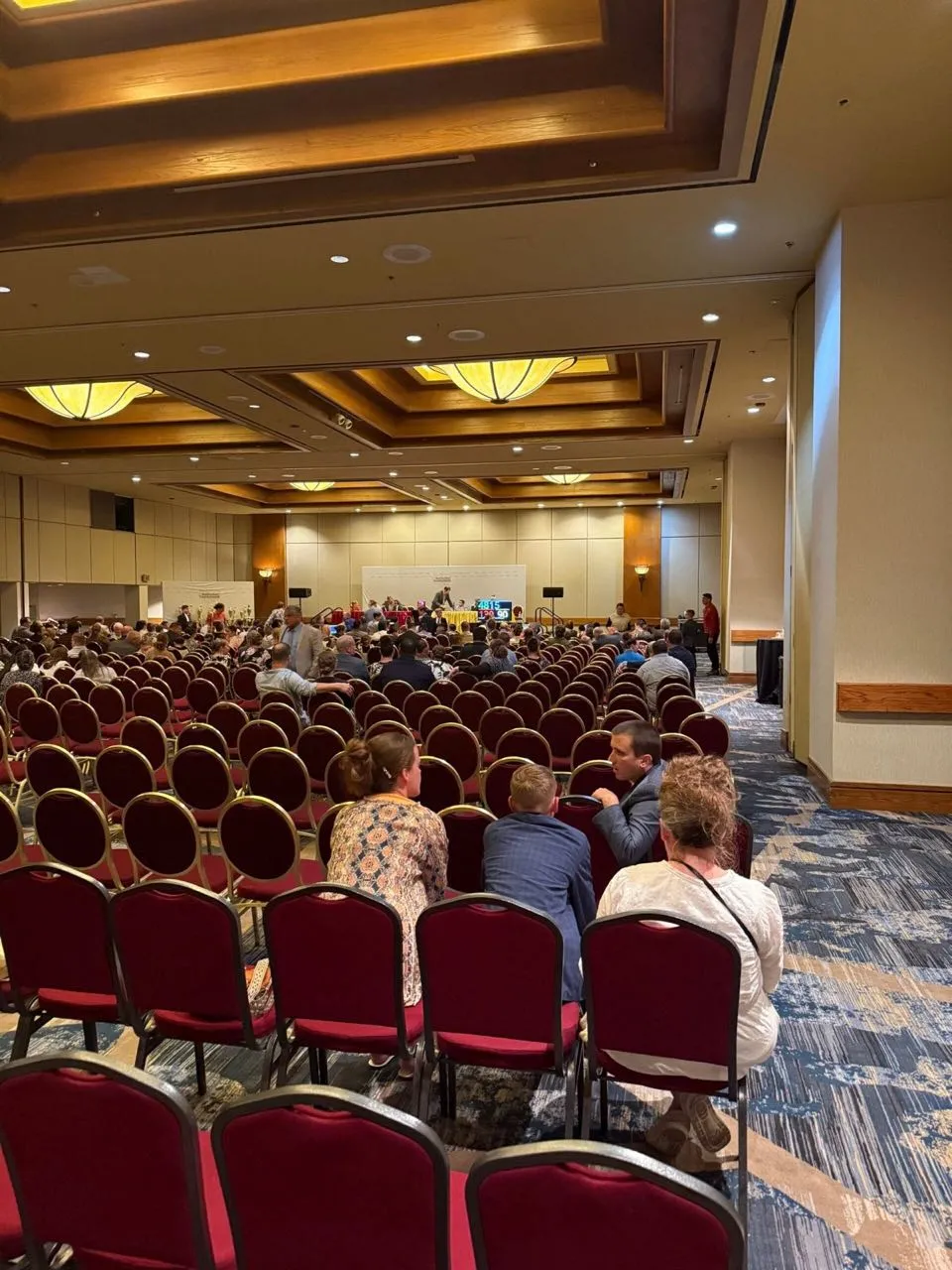 Conference attendees seated in a hotel ballroom during a corporate session with A/V support