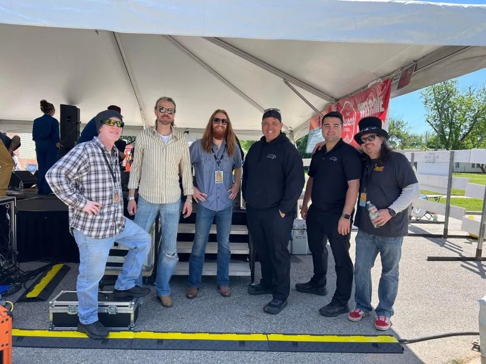 Band members and Phase 3 Live crew posing together under a festival tent