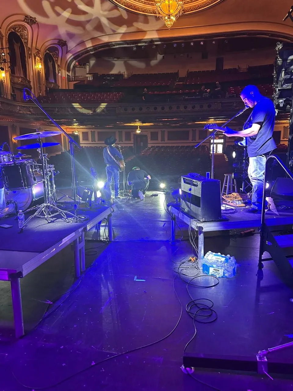 Band soundcheck on a historic theater stage produced by Phase 3 Live, viewed from behind the drum riser.
