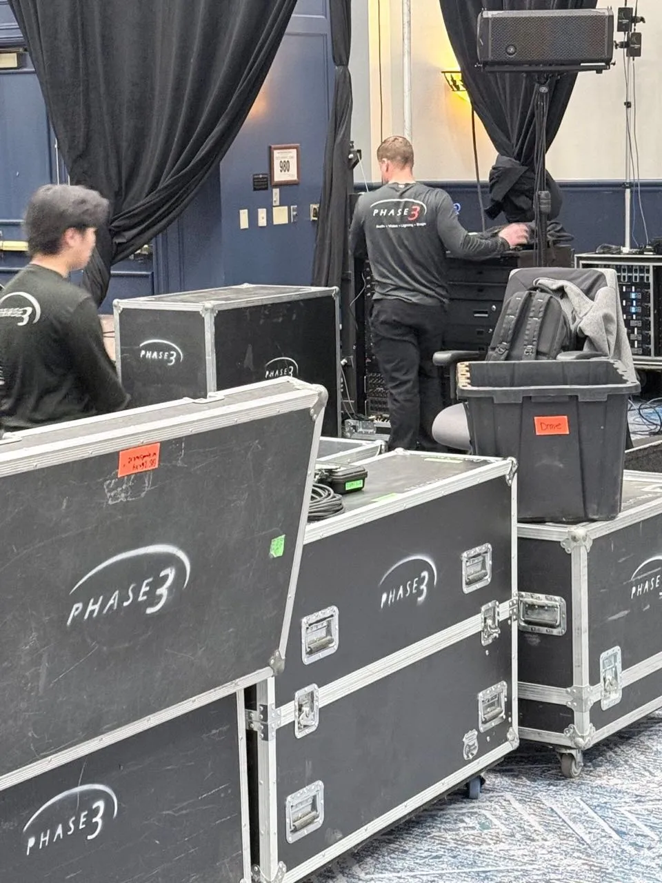 Road cases stenciled with the Phase 3 logo during event setup by the Phase 3 Live crew