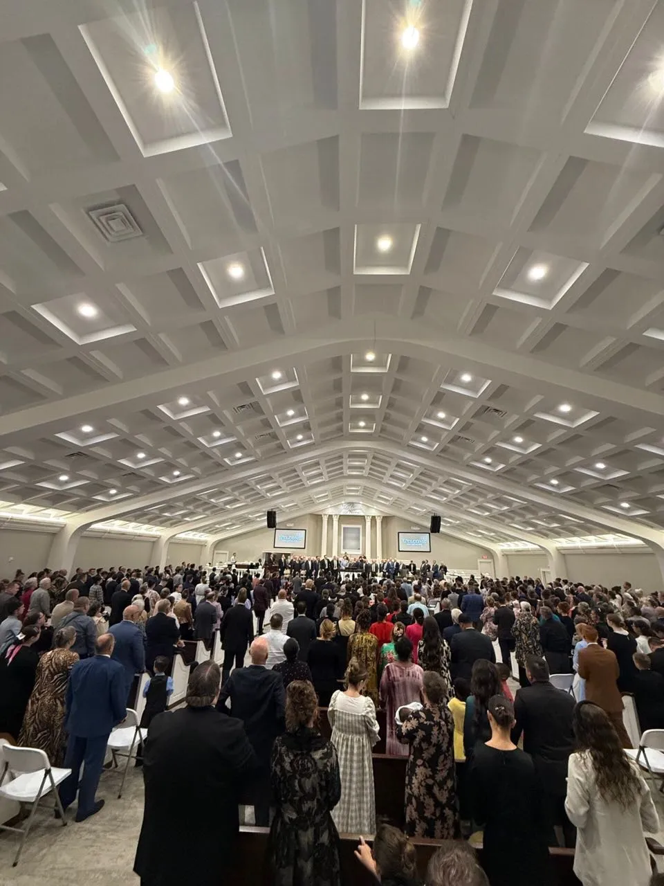 Congregation standing in a large church sanctuary during a service with screens and sound support