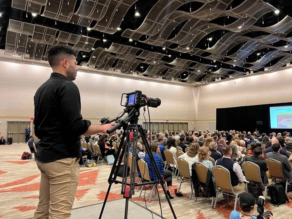 Phase 3 Live camera operator filming a conference session with a broadcast camera on a tripod