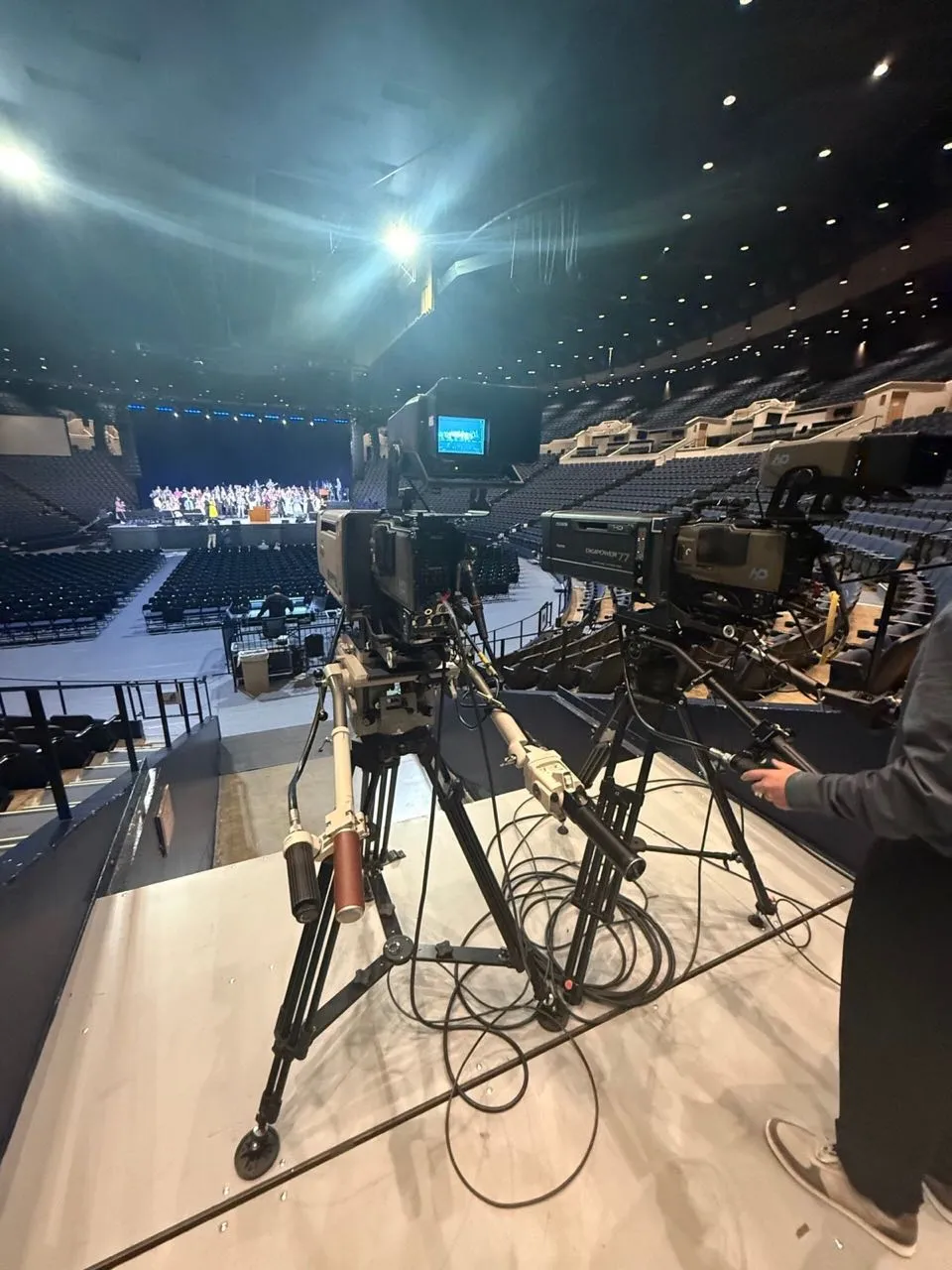Broadcast cameras covering a choir rehearsal on an arena stage during a Phase 3 Live production