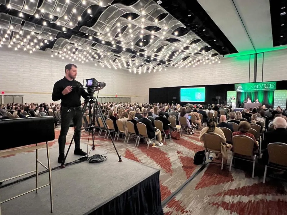 Phase 3 Live camera operator filming a packed conference general session from a riser platform