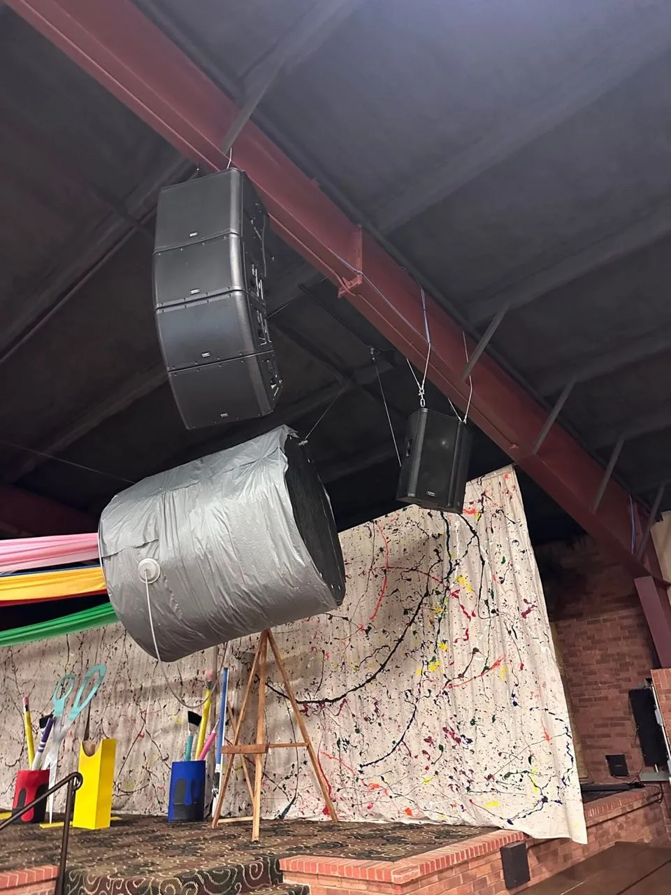 Line array and point-source speakers rigged from the ceiling above a stage by Phase 3 Live