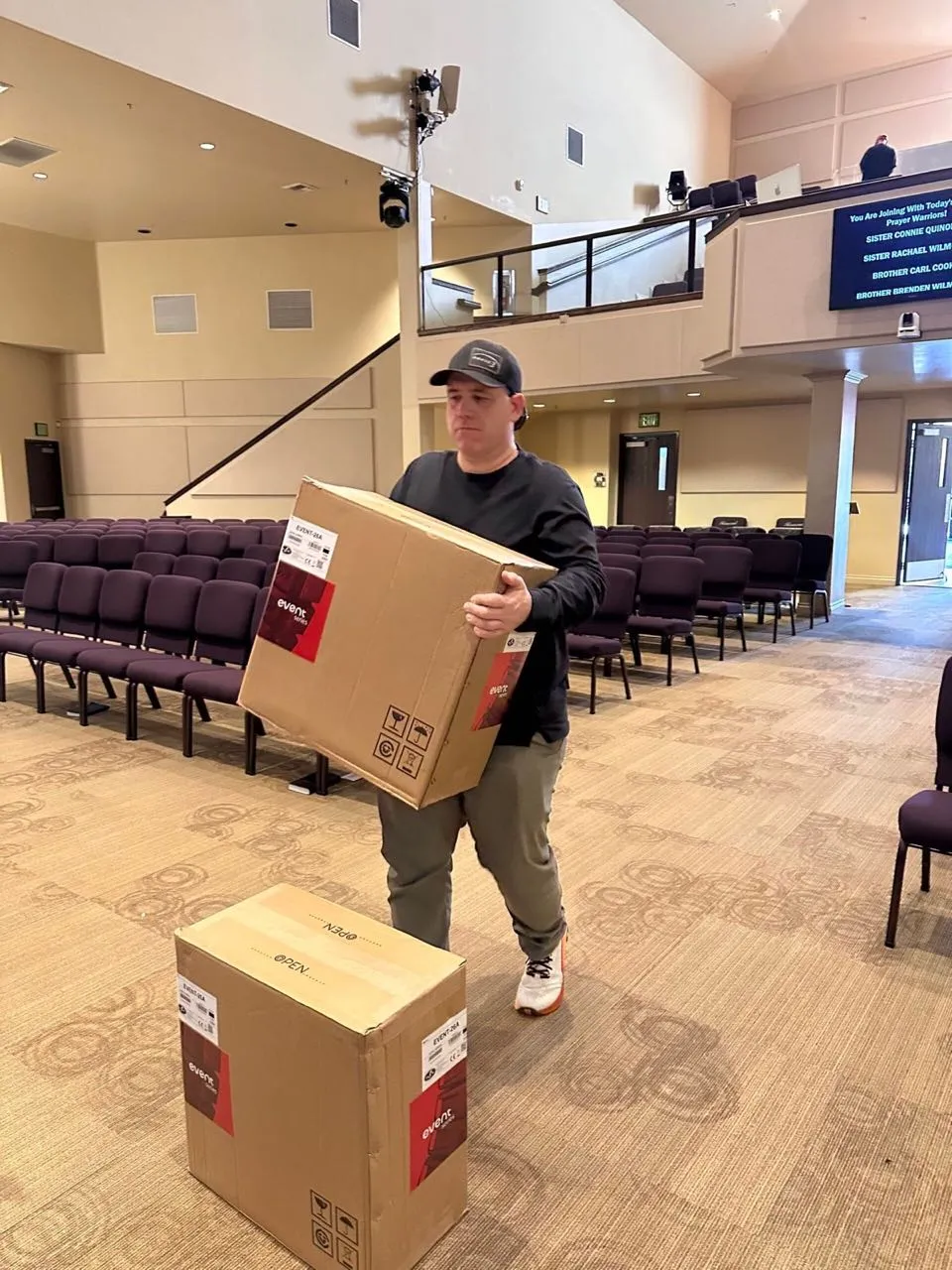 Crew member carrying new speaker boxes into a church auditorium for a Phase 3 Live equipment installation.