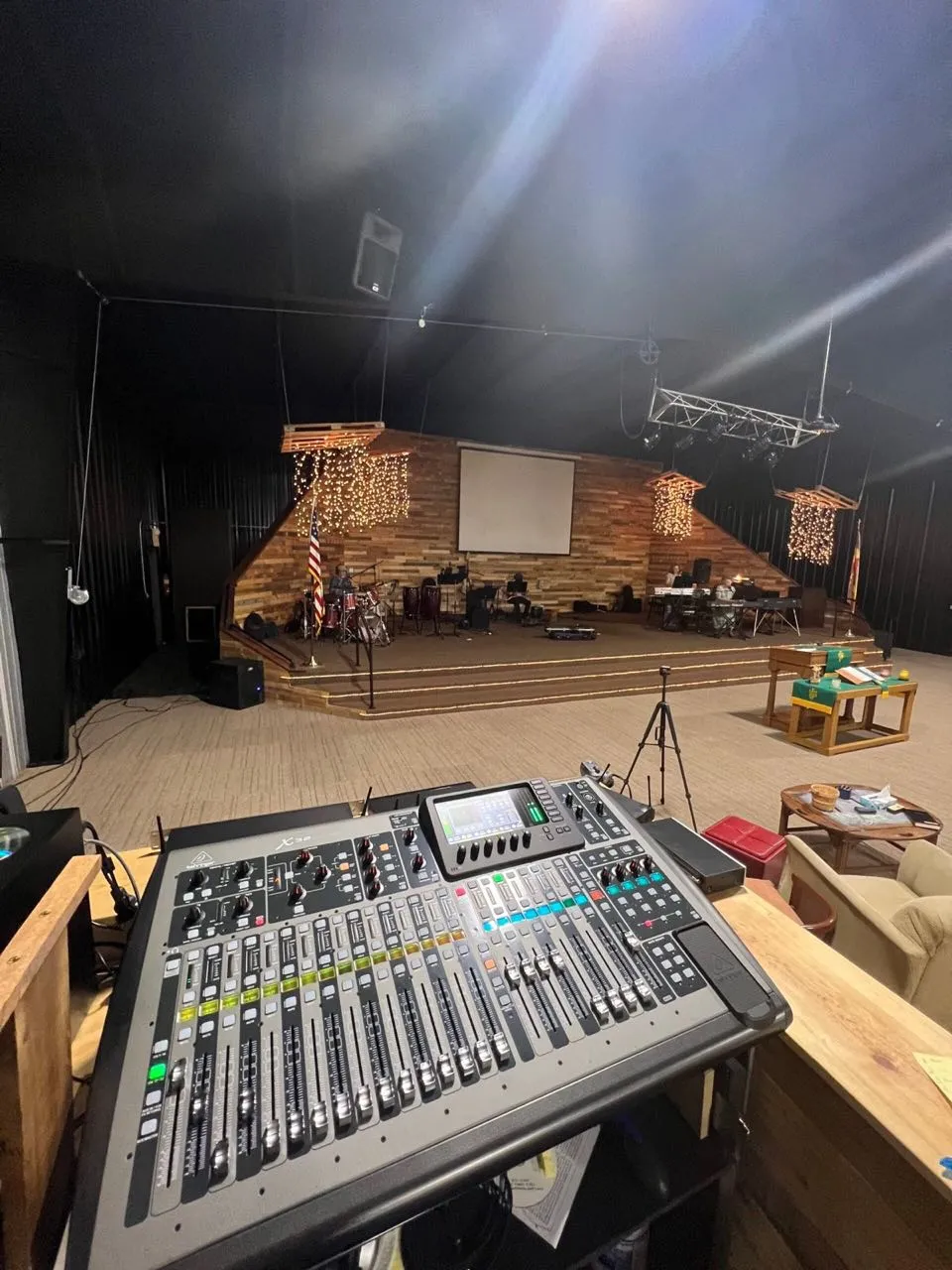 Front-of-house mixing console facing a church stage with band gear and string lights