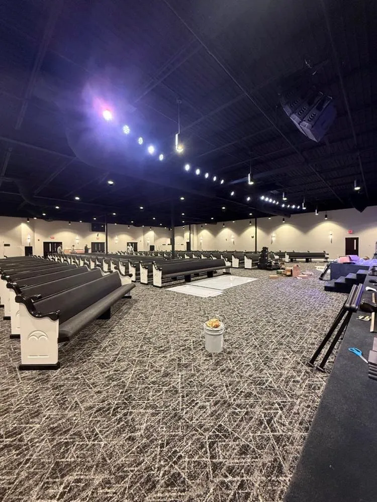 Church sanctuary during an audio-visual installation by Phase 3 Live, with flown line array speakers above rows of new pews.