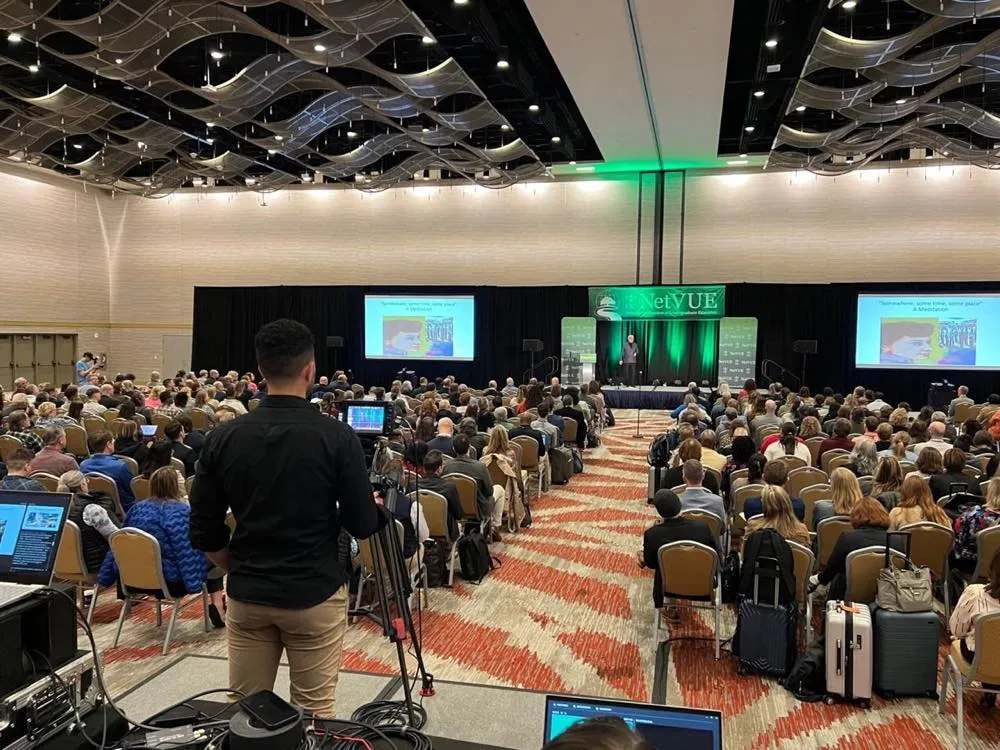 Packed conference general session with dual projection screens and stage lighting produced by Phase 3 Live