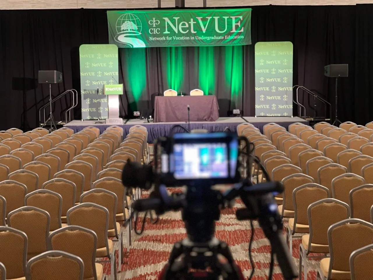 Video camera set up by Phase 3 Live facing a green-lit conference stage before attendees arrive