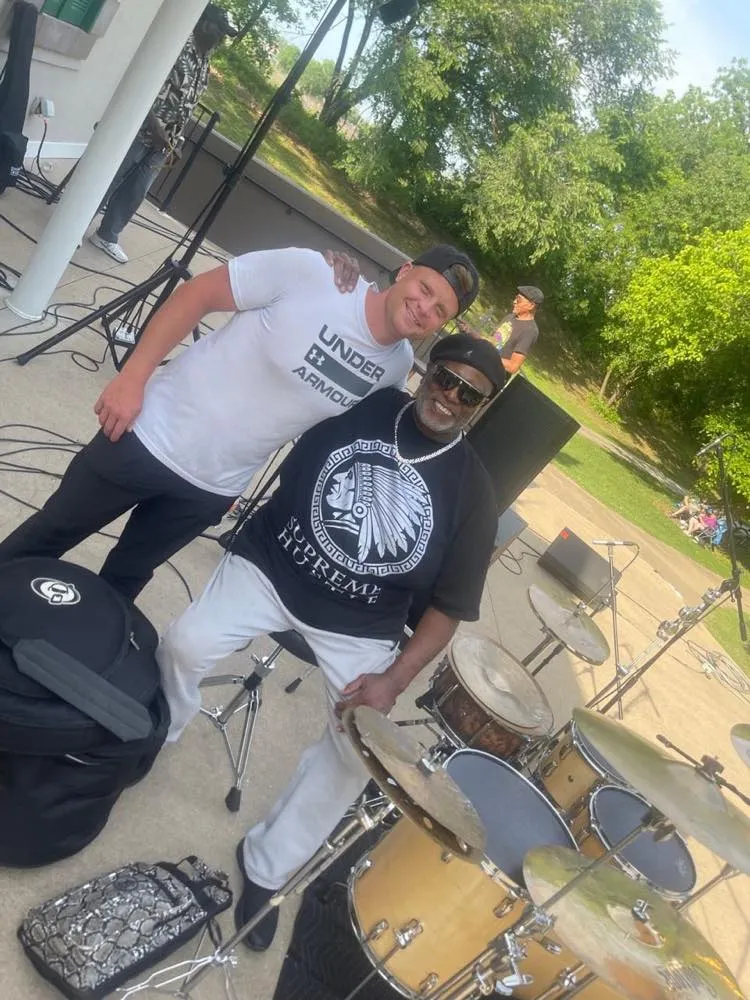Crew member and performer posing by the drum kit at an outdoor event supported by Phase 3 Live