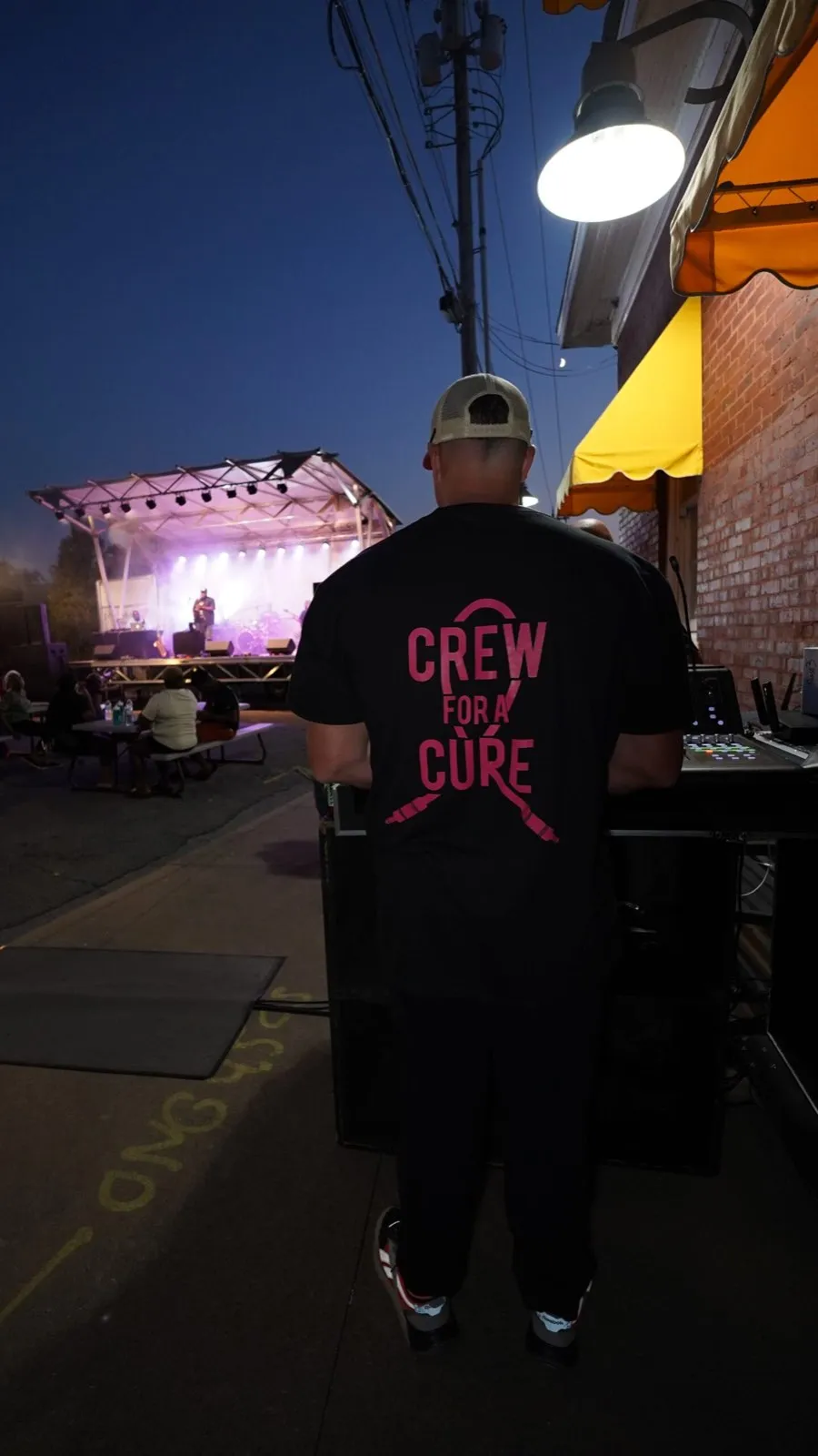 Phase 3 Live sound engineer in a Crew for a Cure shirt mixing an outdoor concert at dusk