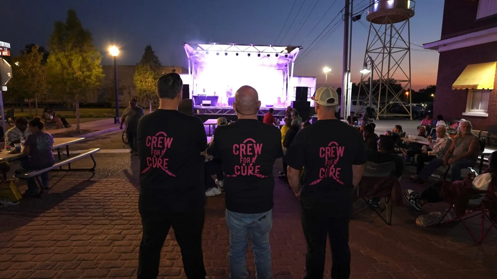 Phase 3 Live crew in Crew for a Cure shirts facing a pink-lit mobile stage at a benefit concert