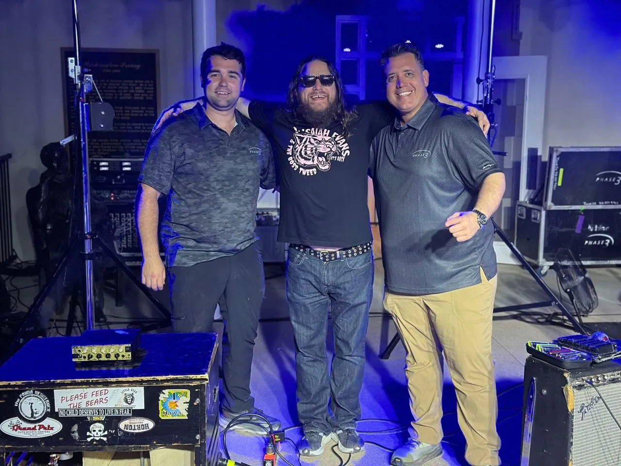 Phase 3 Live crew members posing with a musician on stage after a show, road cases in the background