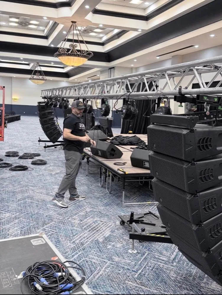Phase 3 Live technician rigging a lighting truss beside the stage during a ballroom event build.