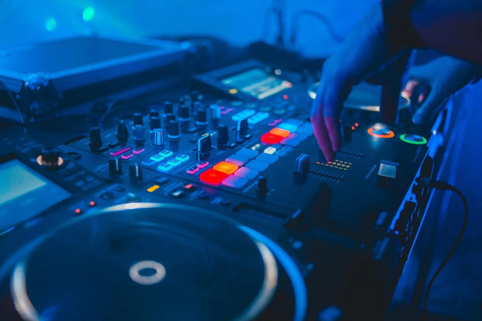 DJ mixing on a controller under blue lighting at a live event