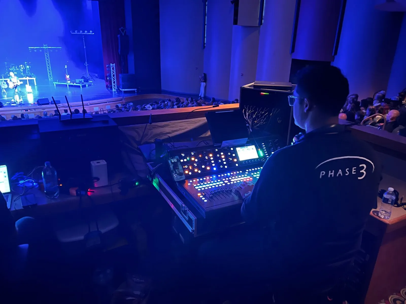 Phase 3 Live engineer mixing front-of-house from the balcony over a packed theater concert