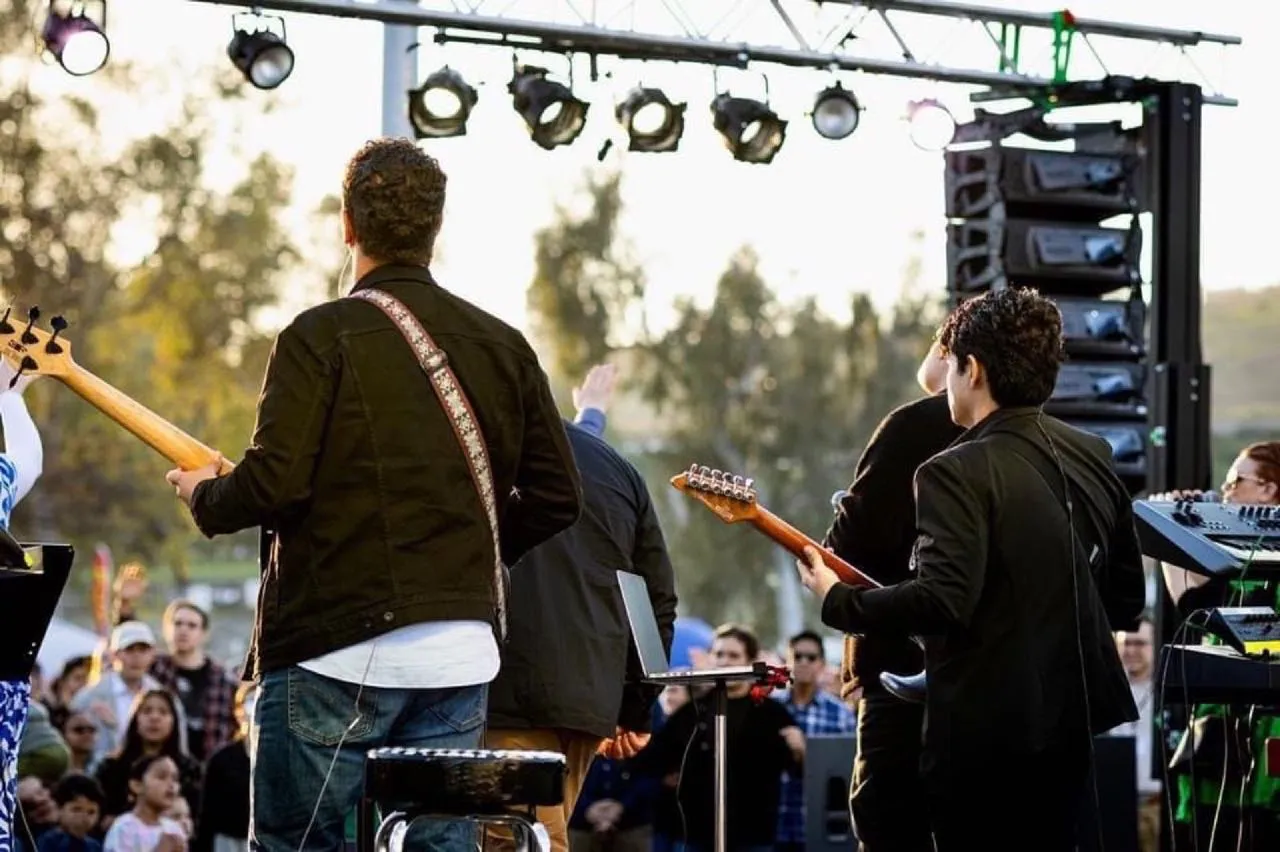 Guitarists perform beneath a Phase 3 Live lighting truss and flown line array at an outdoor event