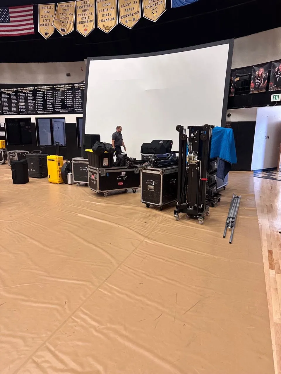 Phase 3 Live road cases, truss lifts, and projection screen during setup in a school gymnasium