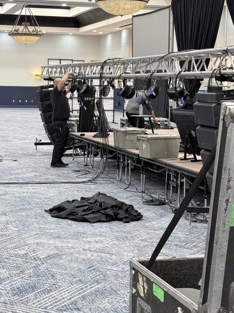 Phase 3 Live technician rigging stage lights on truss during a ballroom event setup