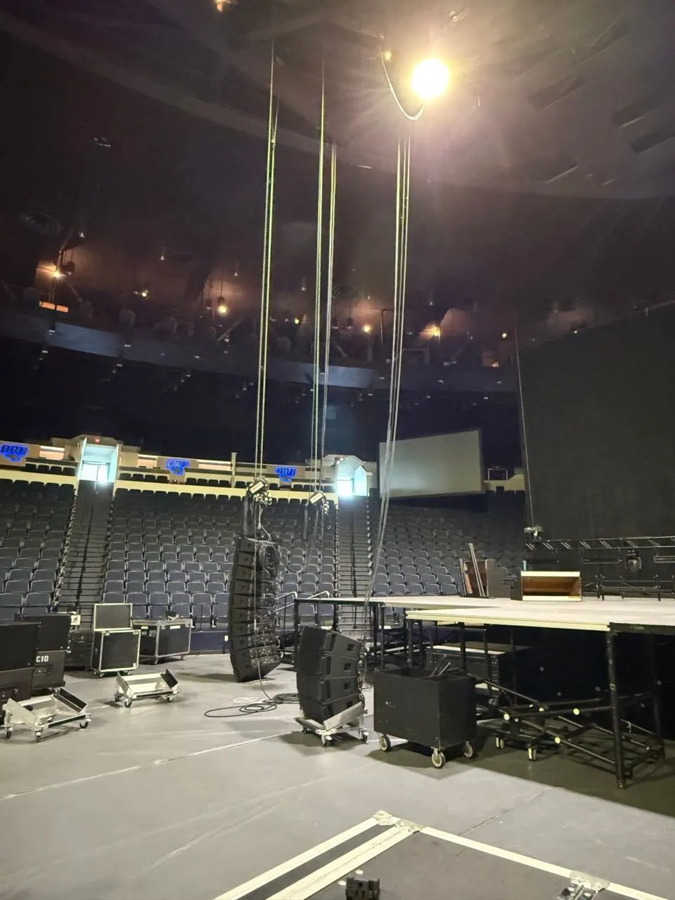 Line array speakers being rigged above an arena floor during a Phase 3 Live concert production load-in