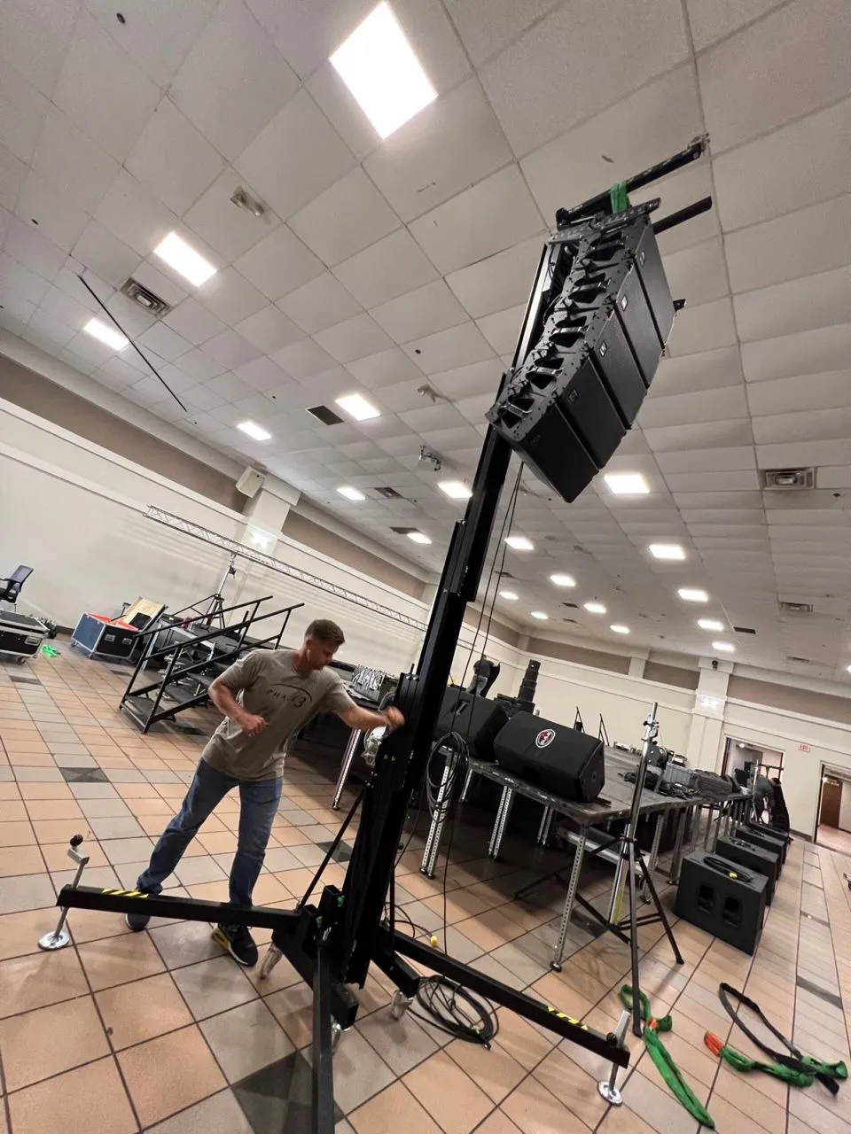 Phase 3 Live technician raising a line-array speaker hang on a crank lift during event setup.