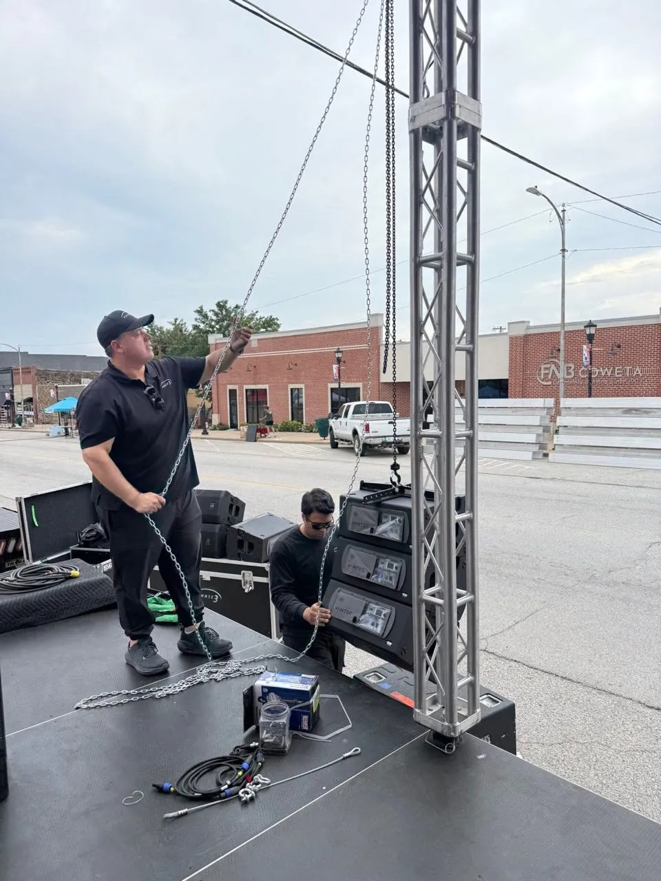Phase 3 Live crew rigging a line-array speaker hang on a truss tower for an outdoor downtown event