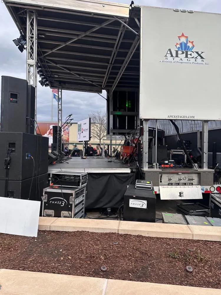 Outdoor mobile festival stage with PA system and Phase 3 Live road cases during setup