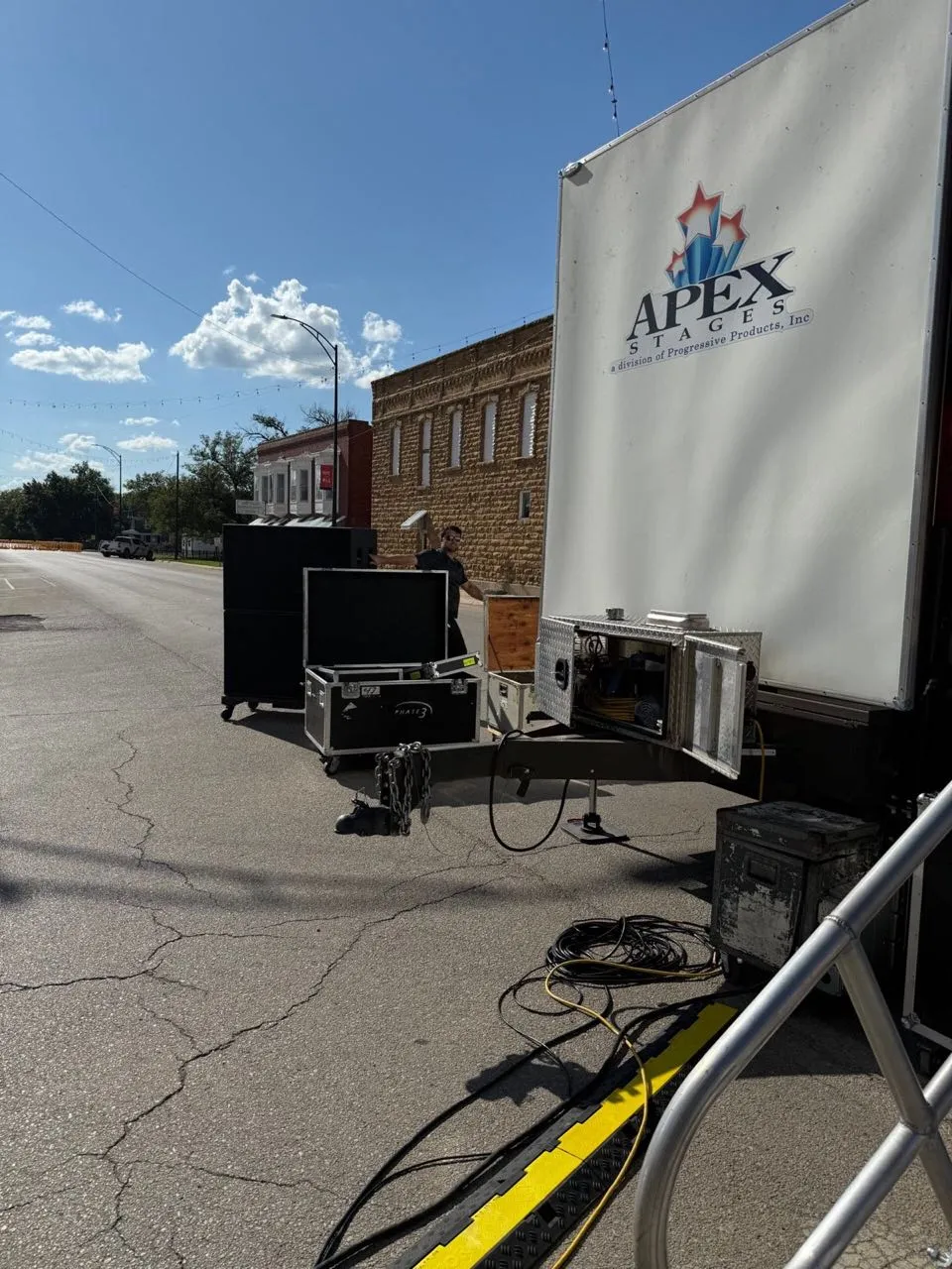 Phase 3 Live crew loading in road cases and speakers at a mobile stage trailer on a downtown street.