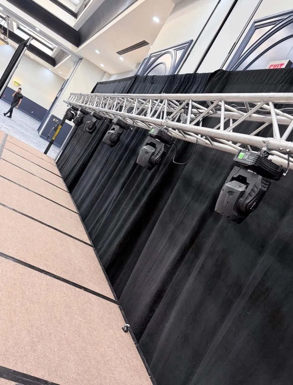 Moving-head stage lights on truss against black pipe and drape installed by Phase 3 Live.