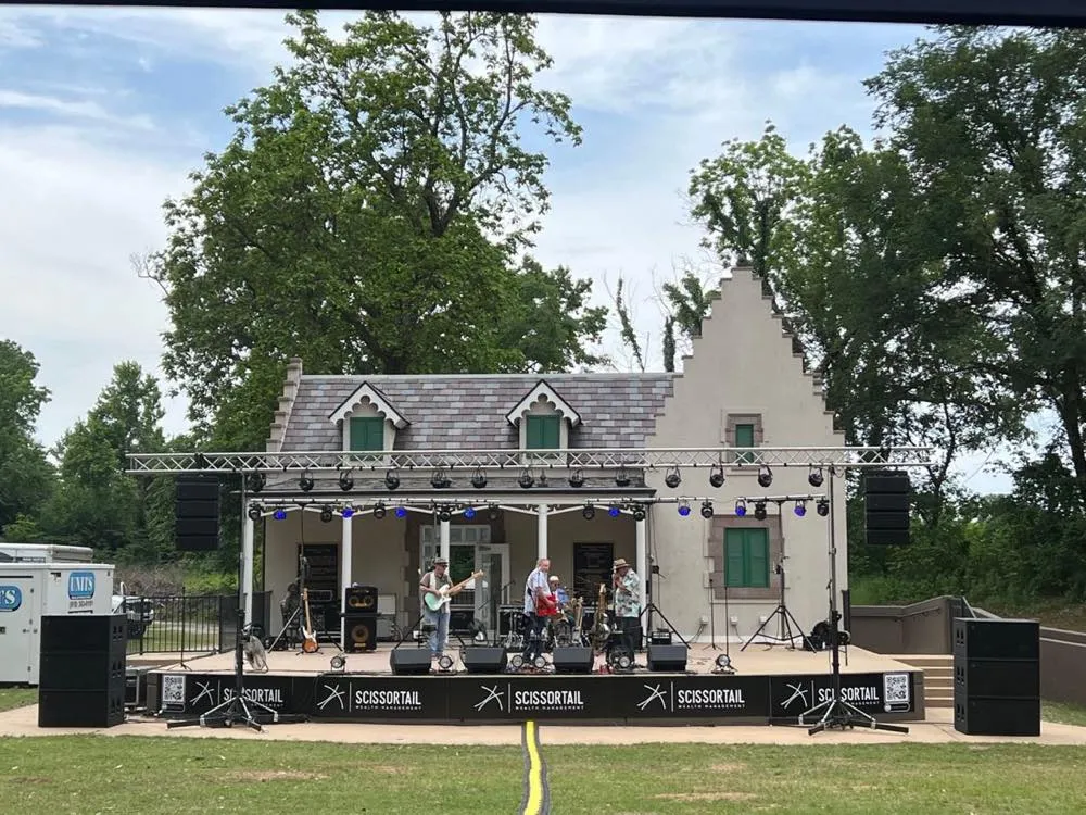 Band performing on an outdoor stage with truss lighting and line arrays produced by Phase 3 Live