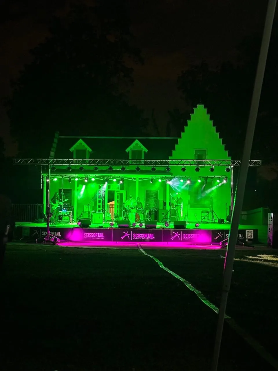 Band performing at night on an outdoor stage with green wash lighting and a truss rig produced by Phase 3 Live
