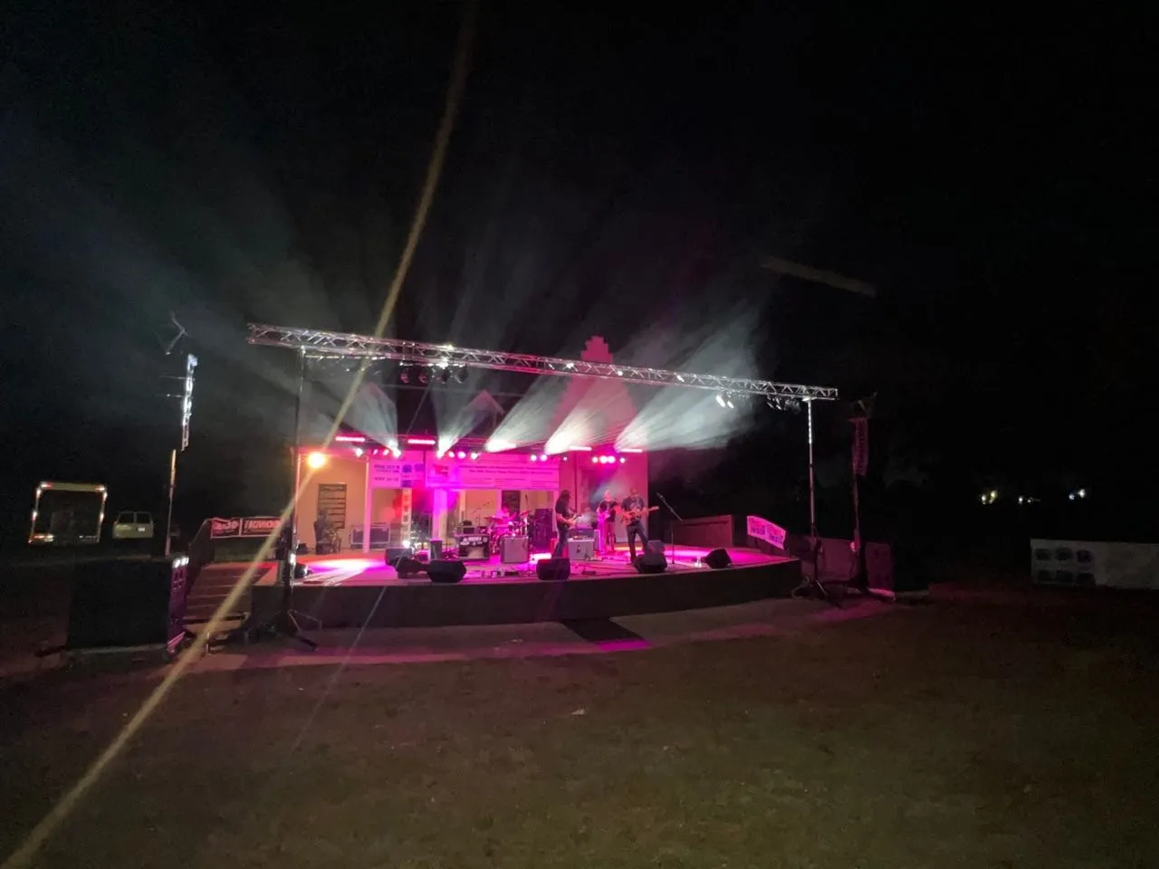 Light beams cut through haze over an outdoor night stage rigged with truss lighting by Phase 3 Live