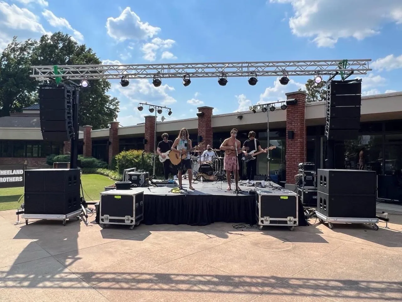 Band performing on an outdoor stage with truss lighting and line-array speakers set up by Phase 3 Live