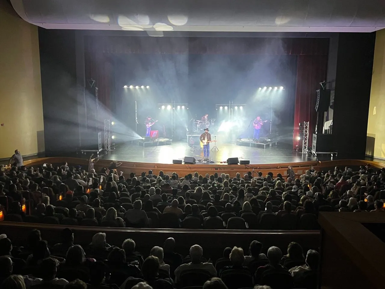 Packed theater crowd watching a band under white stage lighting at a Phase 3 Live concert production