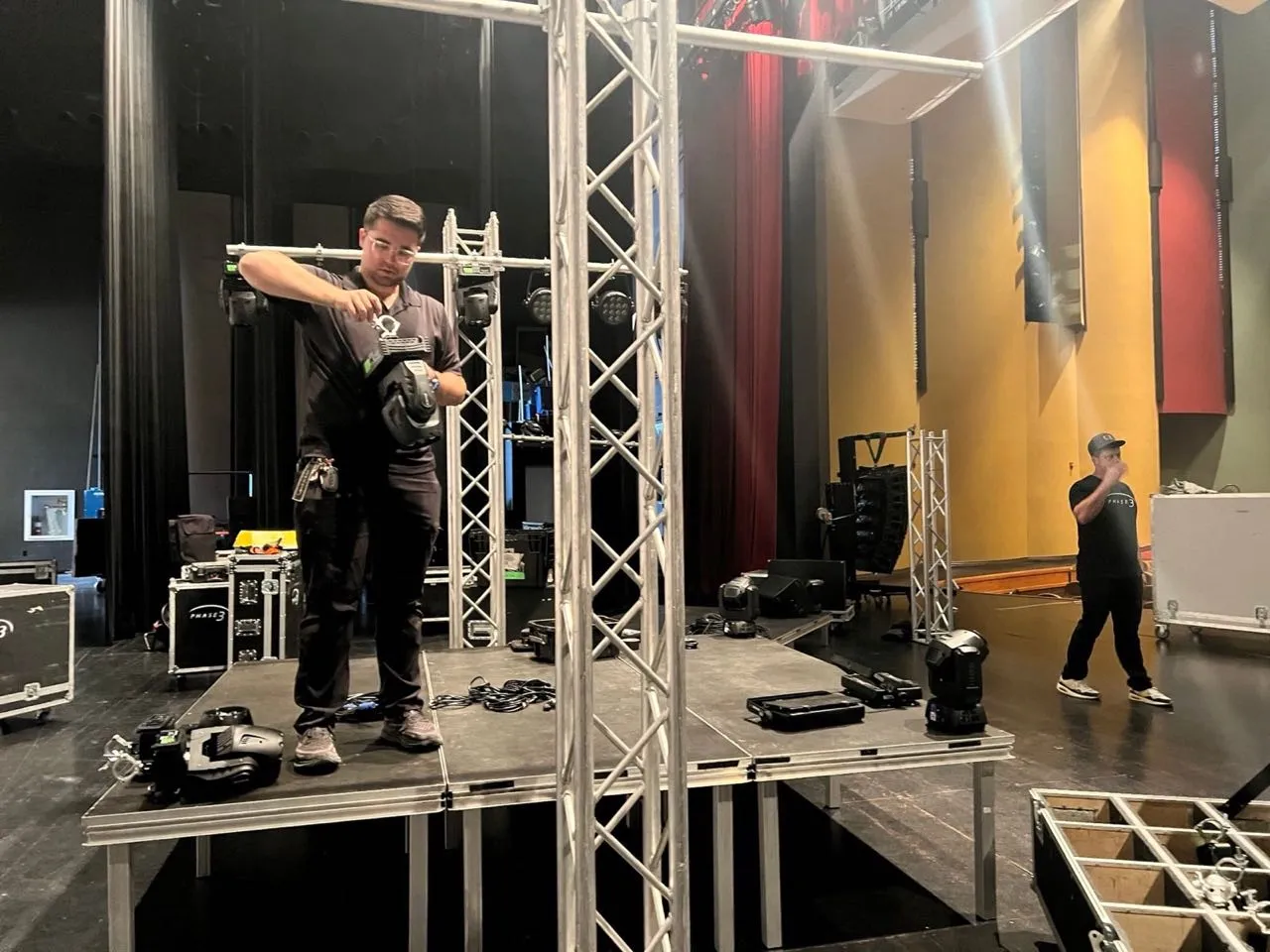 Phase 3 Live technician rigging moving-head lights on truss during an event load-in
