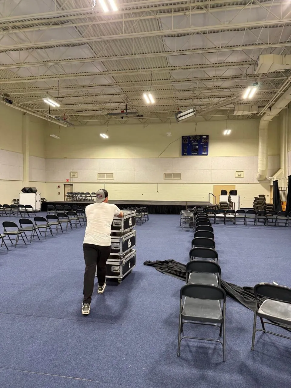 Crew member rolling a stack of road cases across a gym floor during Phase 3 Live event setup