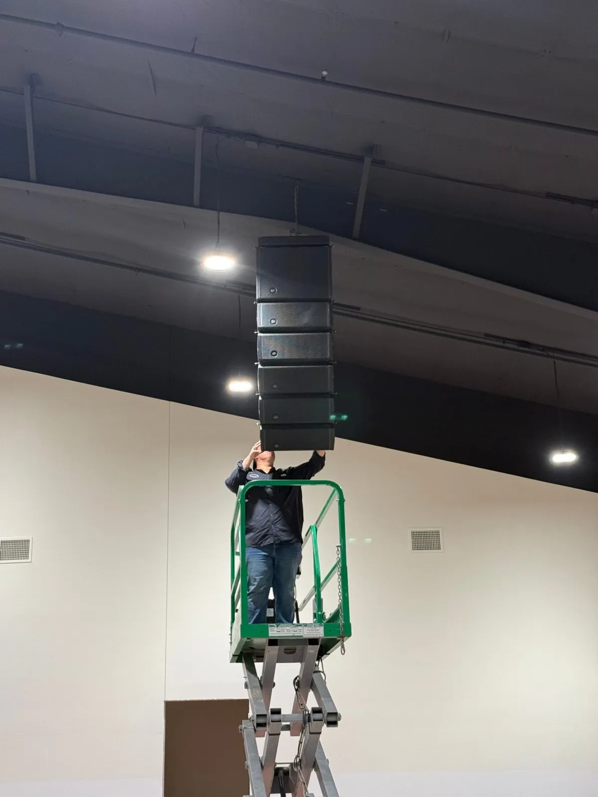 Phase 3 Live technician on a scissor lift installing a flown line array speaker column