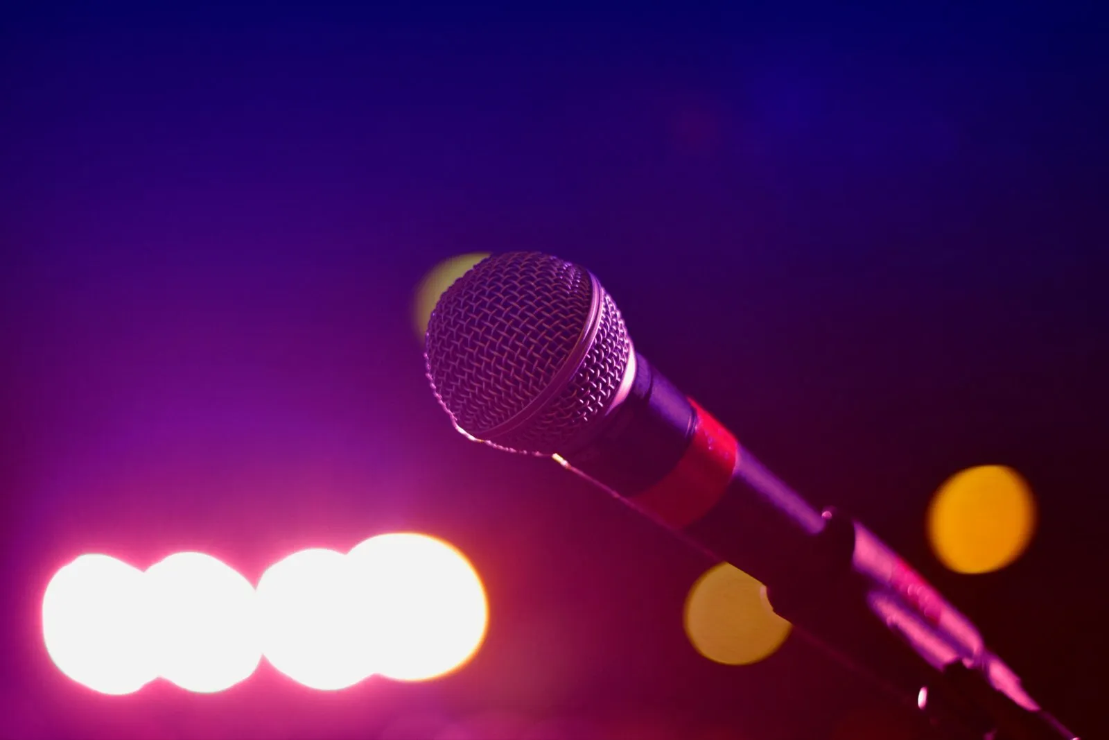 Vocal microphone on a stand with colorful blurred stage lights behind it