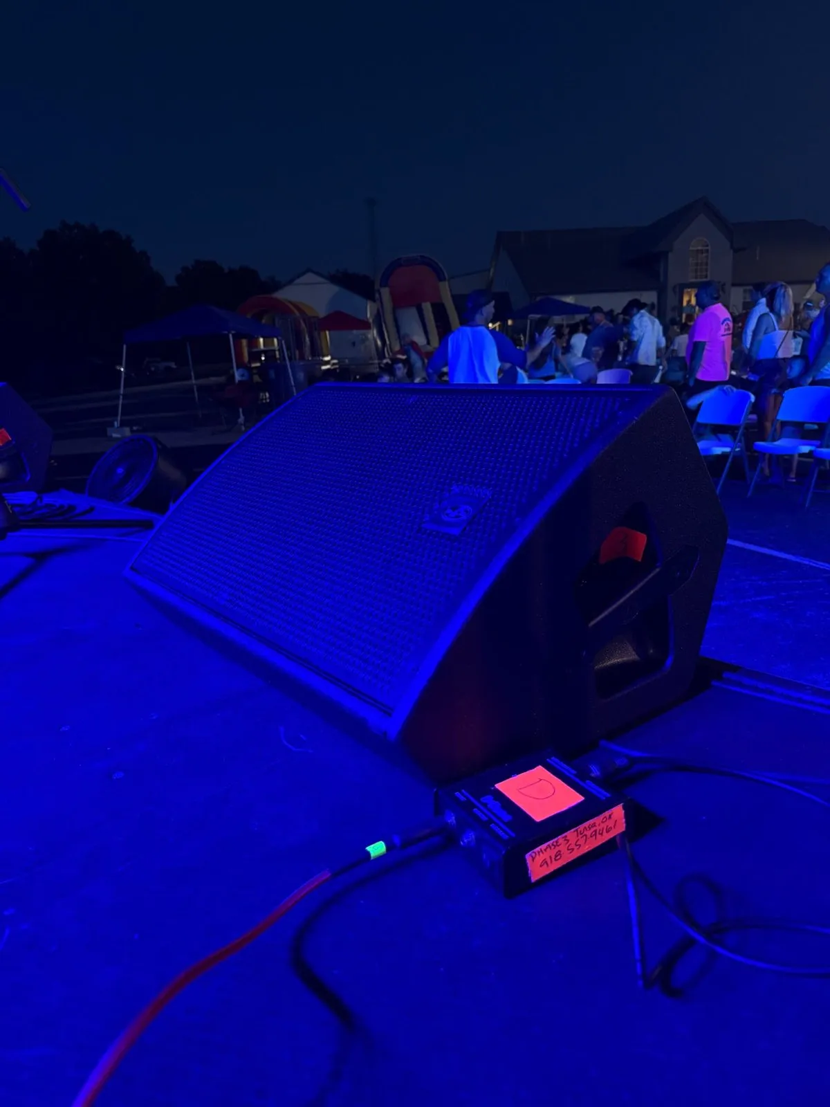 Phase 3 Live stage monitor and labeled DI box on a blue-lit stage at a night community event