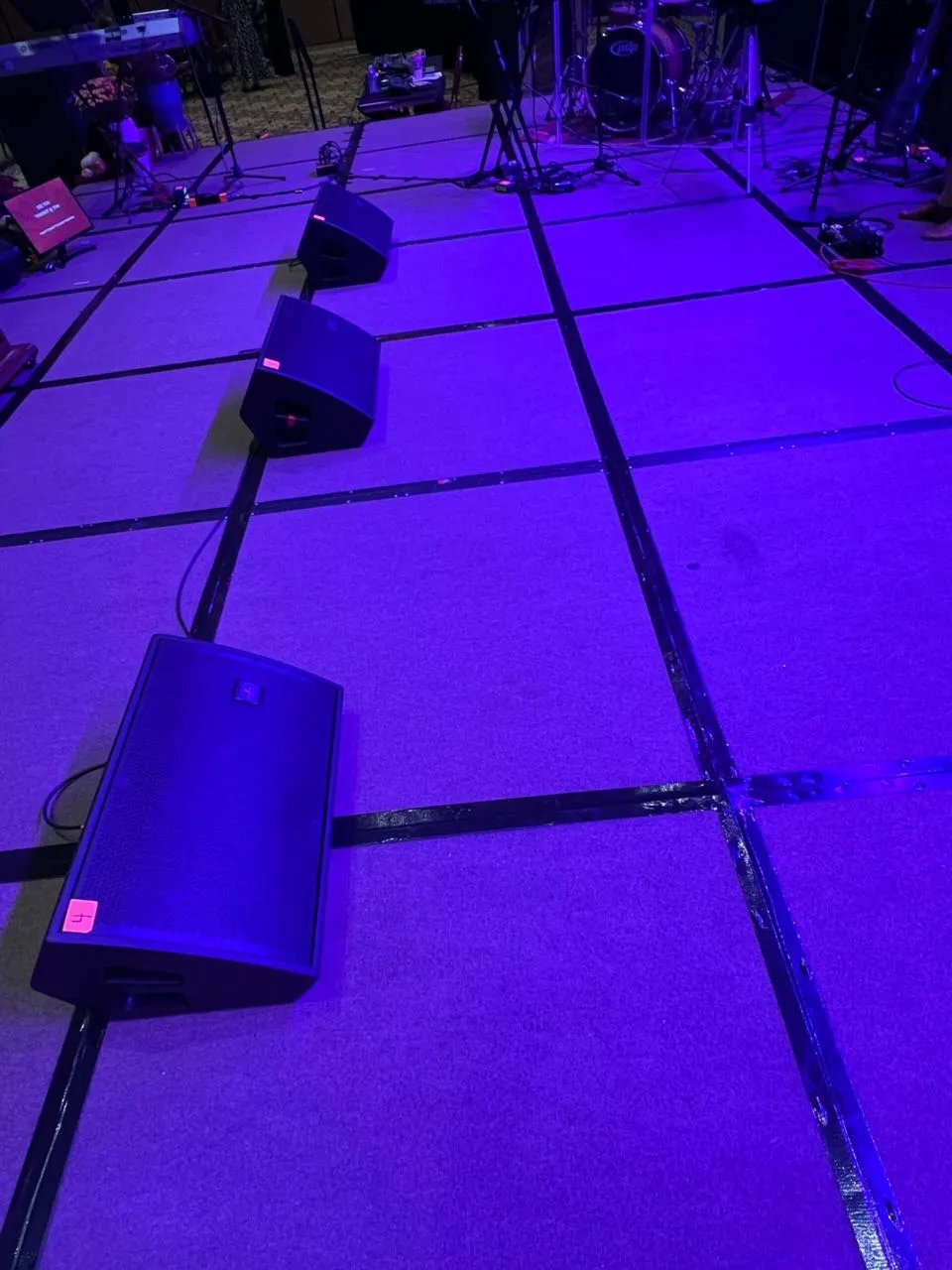 Stage monitor speakers lined across a purple-lit stage deck supplied by Phase 3 Live