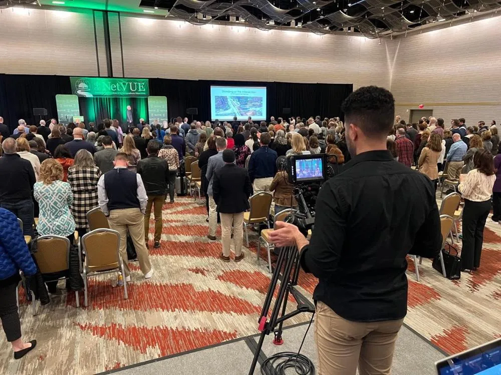 Standing conference audience filmed by a Phase 3 Live camera operator during a general session
