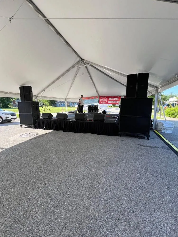 Outdoor festival stage under a white tent with stacked PA speakers supplied by Phase 3 Live
