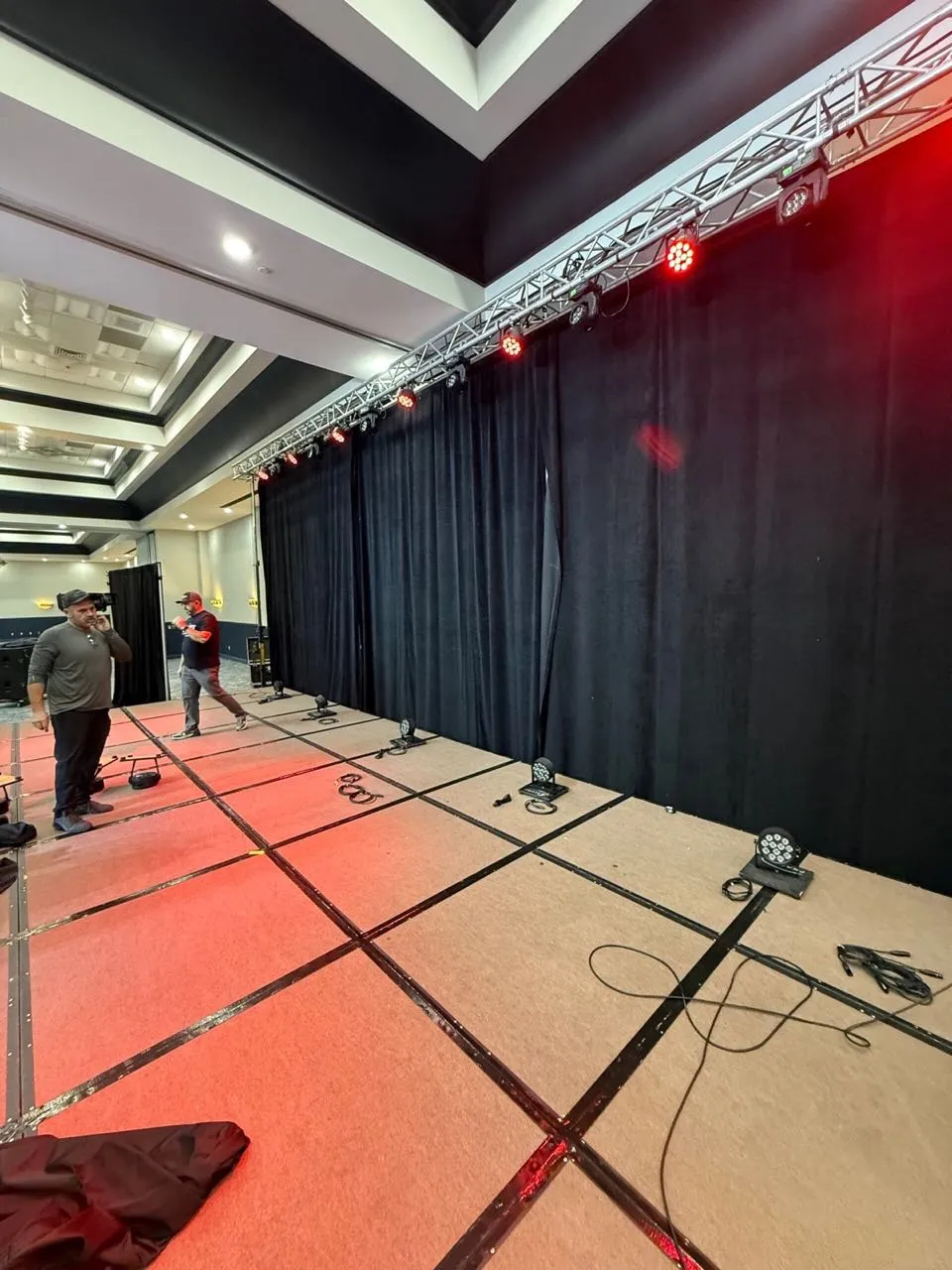 Truss-mounted stage lighting and pipe and drape being set by the Phase 3 Live crew in a hotel ballroom.