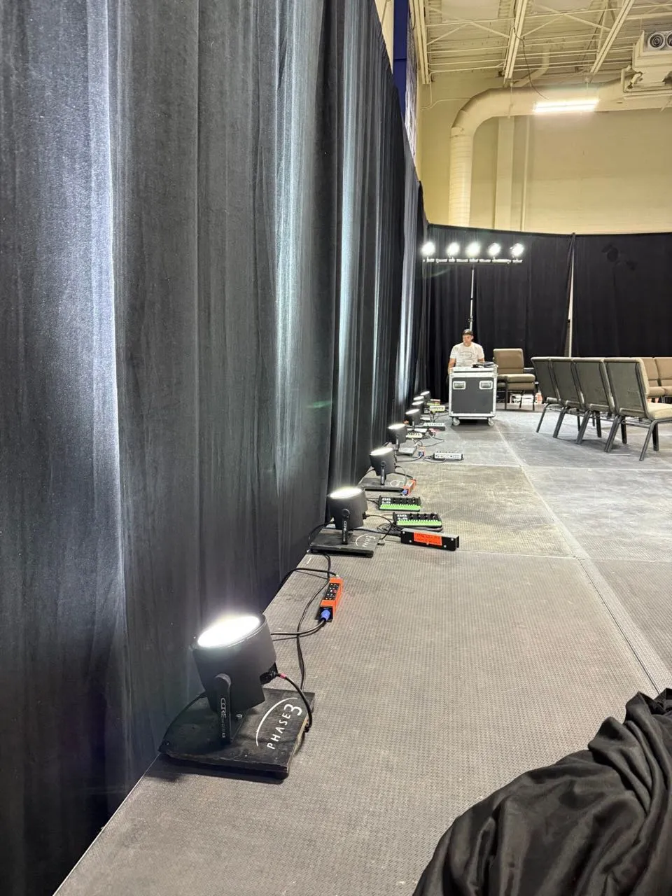 Row of Phase 3 Live uplights along a black drape wall during event setup