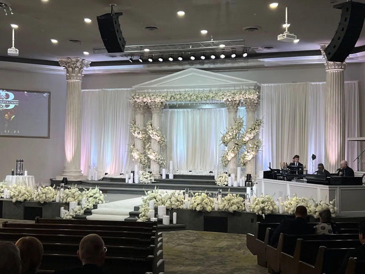 Wedding ceremony staging with white columns, floral pergola, and candlelight produced by Phase 3 Live